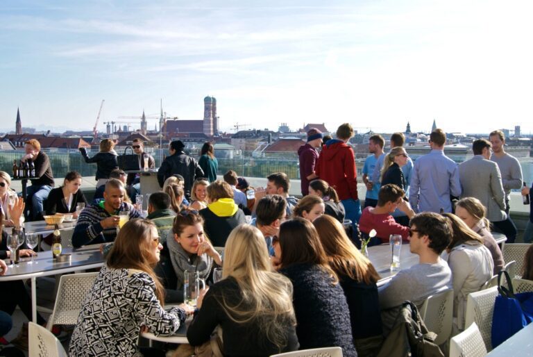 People enjoying food and drinks on a rooftop terrace with Munich city view