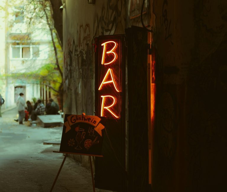 Neon bar sign glowing in a graffiti-covered alley with cozy outdoor seating