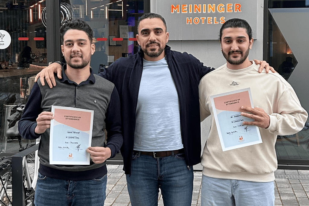 Mohammed in der Mitte umarmt Isaam und Ali, die vor dem Hotel ihre Urkunde zeigen