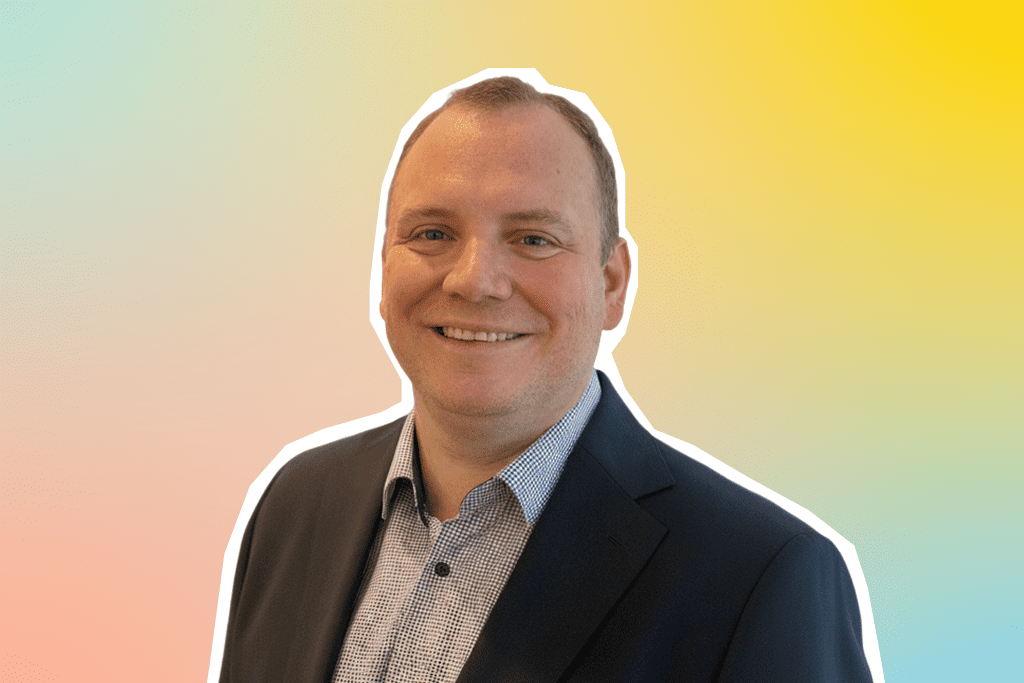 Ein Porträt von Tobias, Senior Area Director Operations bei MEININGER Hotels, vor einem bunten Hintergrund