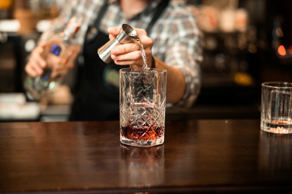 Cool bars in Frankfurt: Bartender pouring clear spirit into glass over red cocktail base