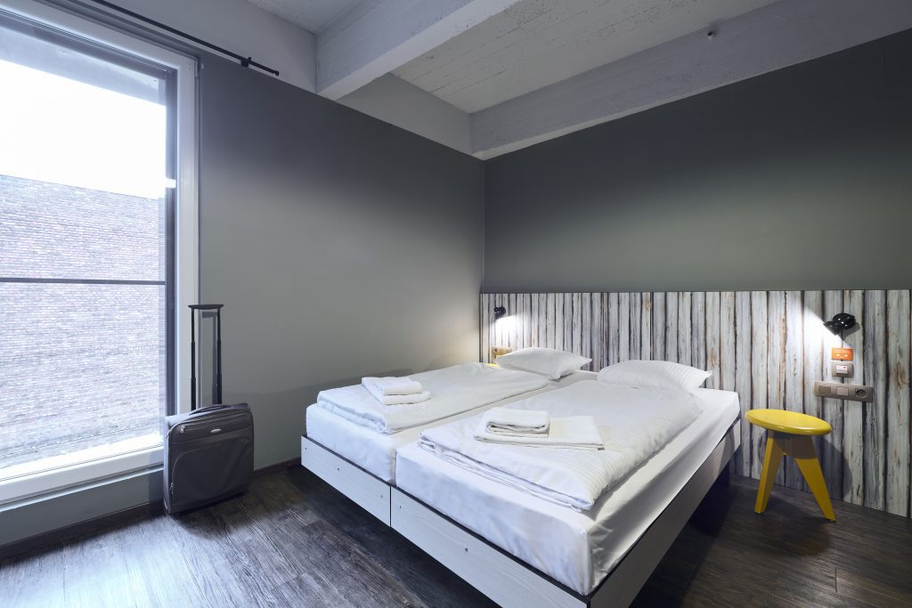 Einfaches Zweibettzimmer mit rustikalem Kopfteil und gelbem Hocker