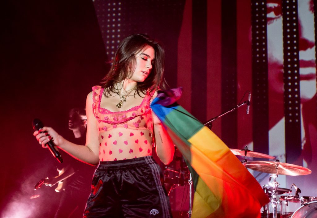 Concerti imperdibili in Europa 2025: Dua Lipa si esibisce dal vivo tenendo in mano una bandiera del Pride durante il suo show