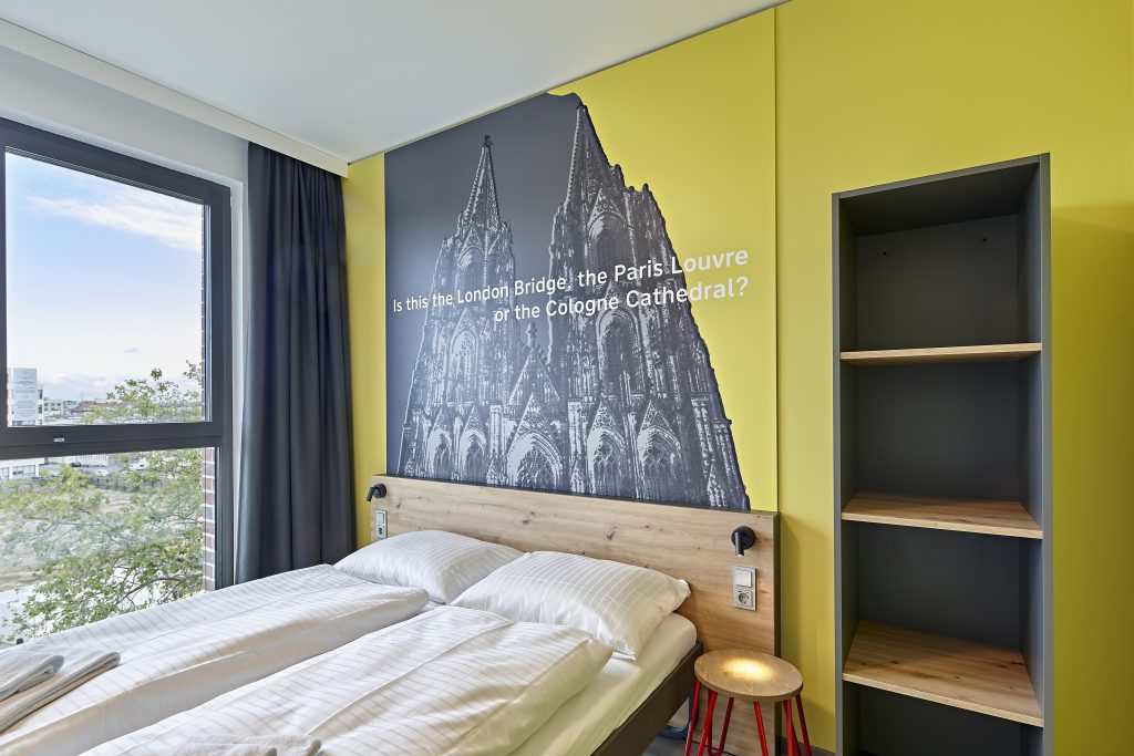 Bright MEININGER Hotel Köln West room with double bed and Cologne Cathedral artwork