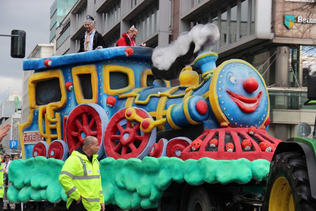 Düsseldorfer Karneval: Bunter Karnevalswagen in Form eines fröhlichen Zugs mit großen Rädern
