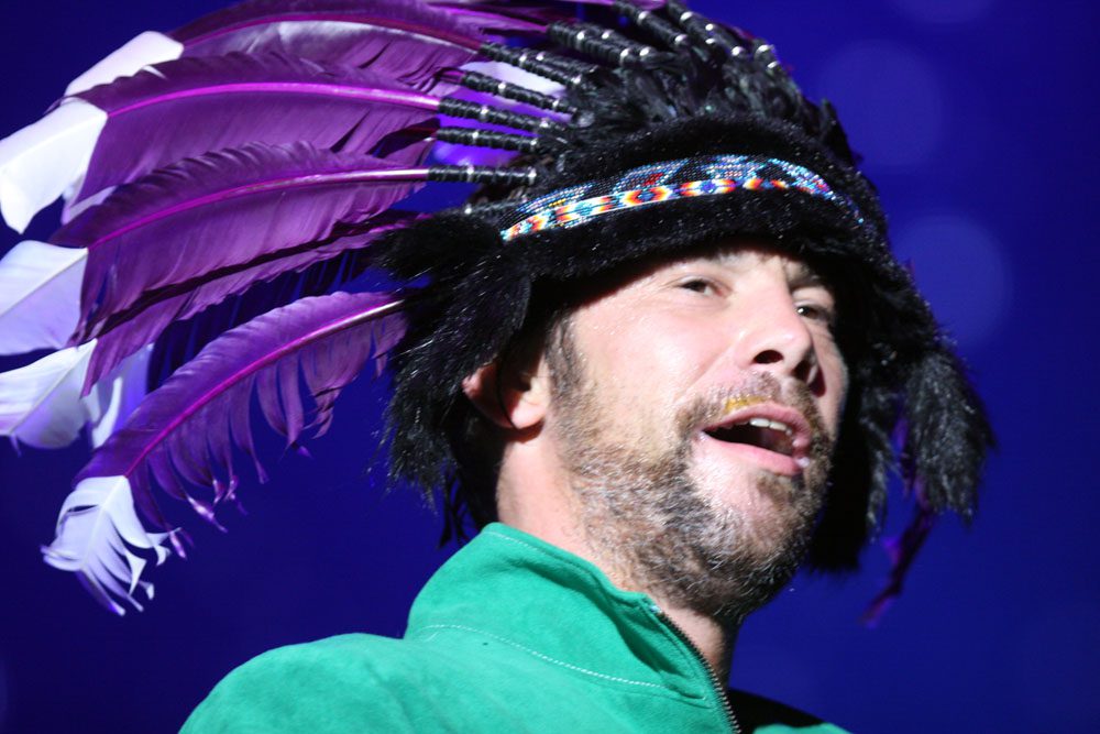 Jay Kay from Jamiroquai rocking his feather hat on stage

