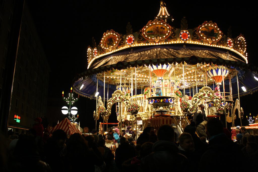 Leipzig Weihnachtsmarkt: Buntes Karussell im Dunkeln – viele Leute feiern auf dem Weihnachtsmarkt.