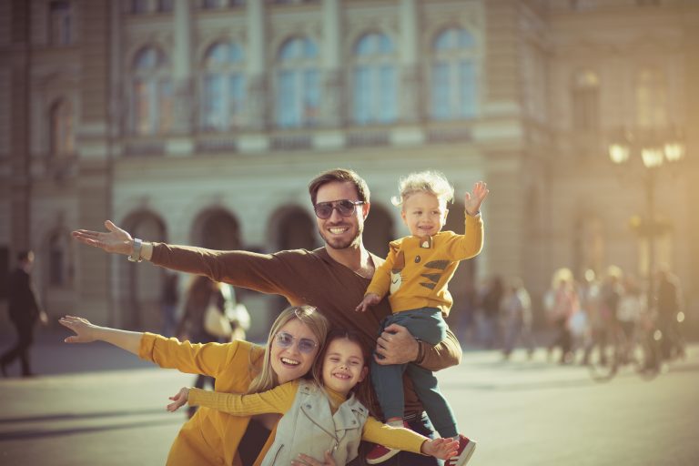 Smiley family of 4 with open arms in front of a city building