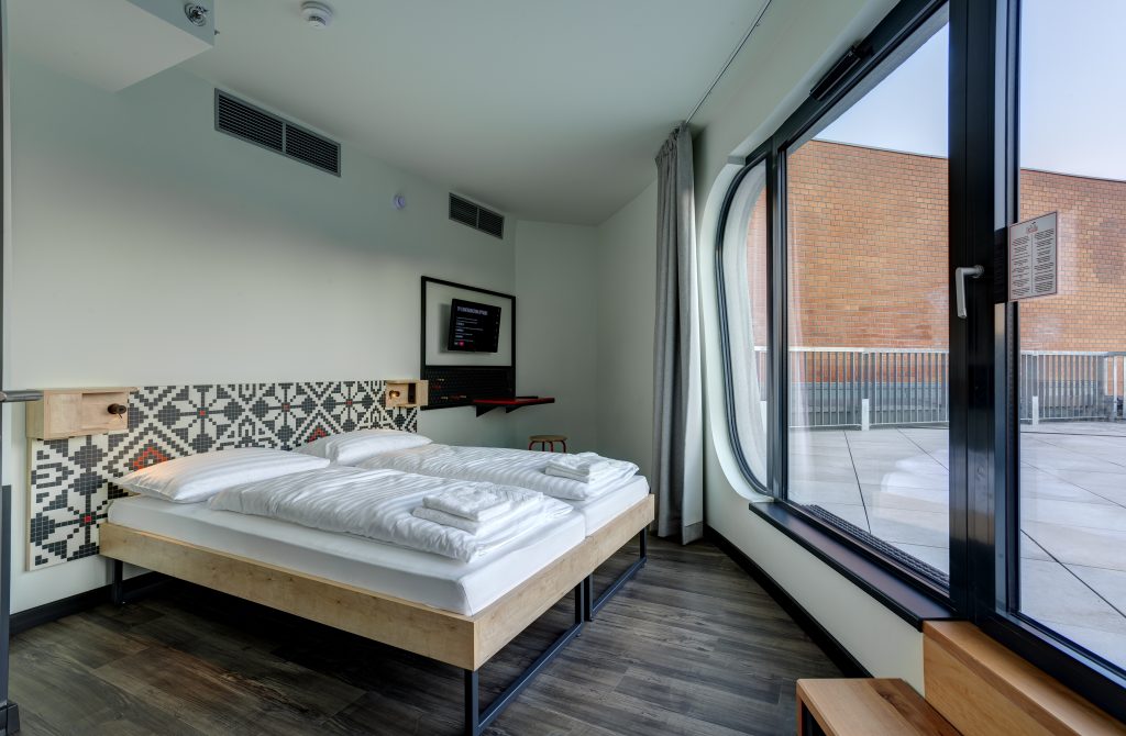 Helles Doppelzimmer mit großem Fenster und stylischer Musterwand im MEININGER Budapest Great Market Hall 