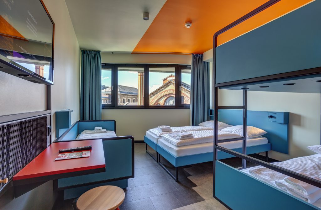 Buntes Mehrbettzimmer mit Etagenbetten und Stadtblick im MEININGER Budapest Great Market Hall 