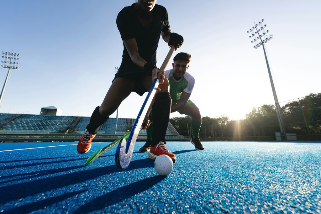 Sportveranstaltungen Europa: Zwei Hockeyspieler kämpfen um den Ball auf blauem Spielfeld 