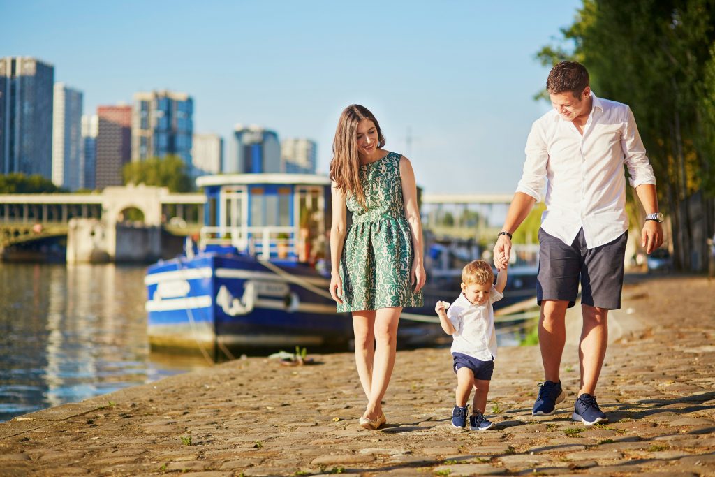 Family trip to Paris: Family walking by the Seine with boats and city skyline in the background
