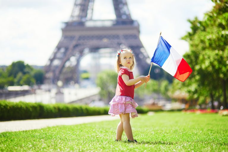 A little girl holding the France flag with the Eiffel tower on the background