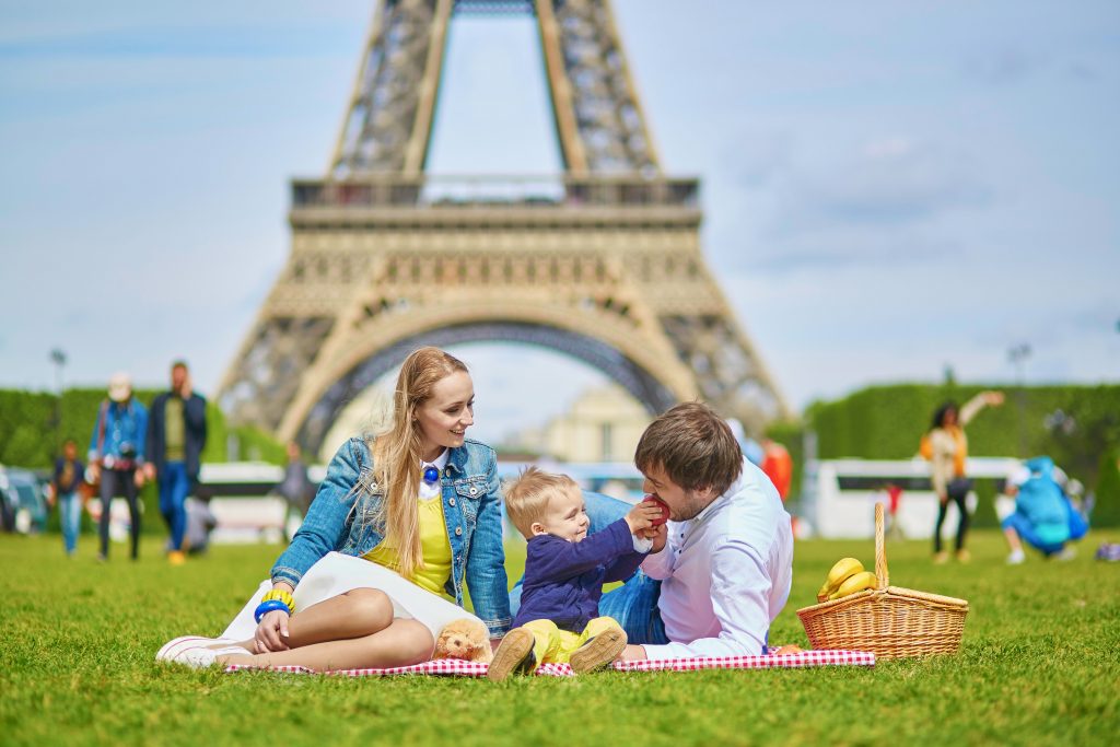 Family trip to Paris: Family picnic on the grass with Eiffel Tower in the background
