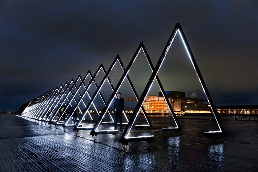 Light festival Copenhagen: a man walking through a glowing triangles sculpture