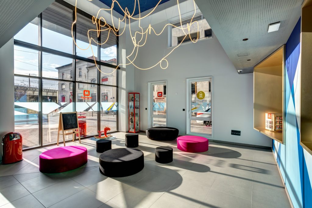 Hall d’entrée coloré avec sièges ronds et grandes fenêtres au MEININGER Hotel Lyon Centre Berthelot
