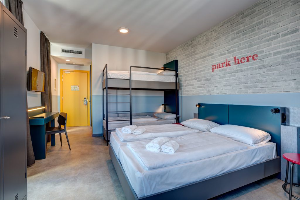 Room with bunk beds and comfy double bed, writing “park here” on the wall