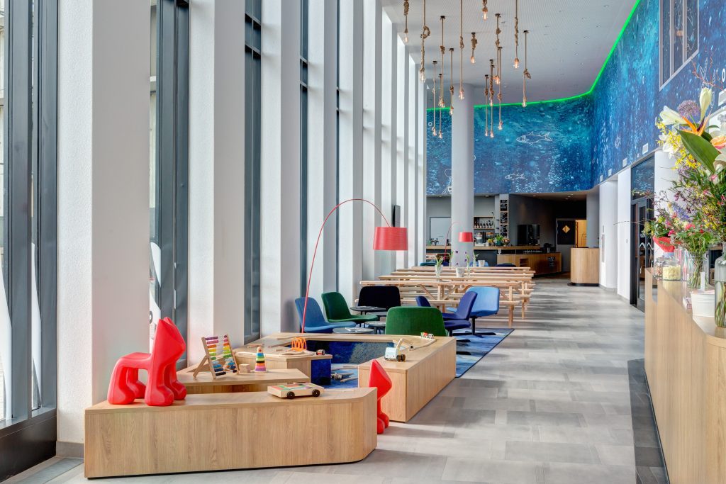 MEININGER Hotel Amsterdam Amstel: hall dell'hotel con murale blu sulla parete, area giochi per bambini, poltrone lounge