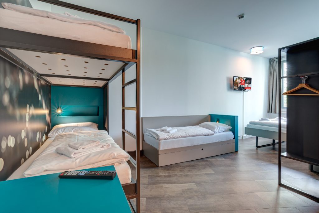 MEININGER Hotel Munich Olympiapark: camera con due letti a castello, un letto singolo e due letti singoli sullo sfondo