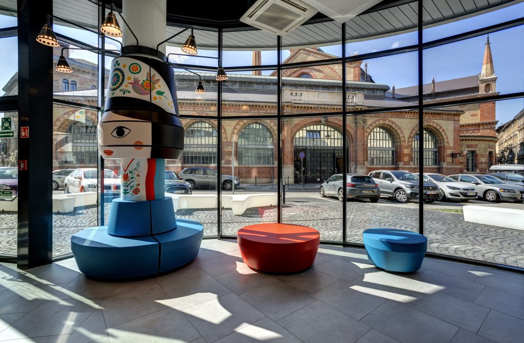 MEININGER Budapest Great Market Hall: hall con panchine di design e statua di una bambola che indossa il costume nazionale ungherese