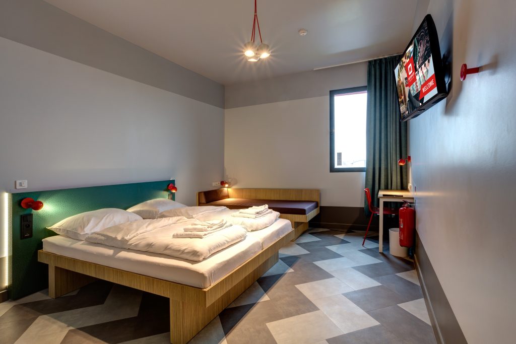 Double room with green bed header and curtain, TV, a desk and a red chair