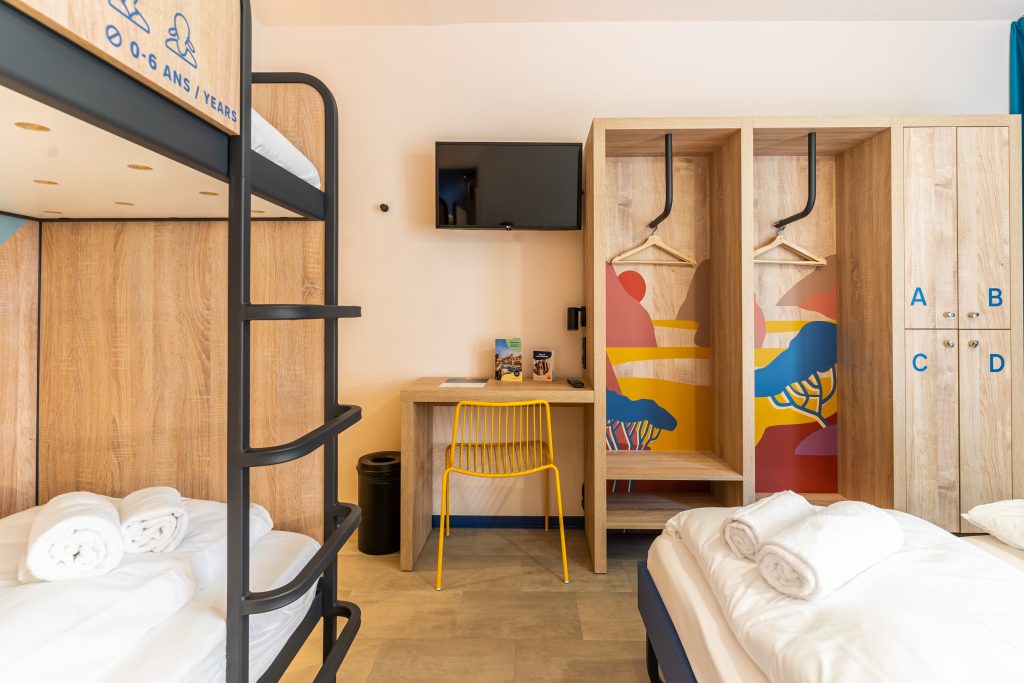 Shared dormitory with wooden bunk beds and wardrobe, decor, TV, a desk and a yellow chair