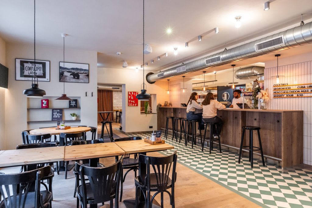 Hotel bar with wooden table and black chairs and stools. Two women at the table bar with a bar tender.