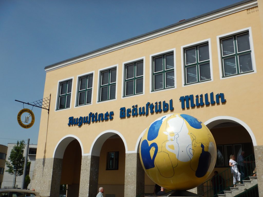 Augustiner Bräu Salisburgo: edificio dell'Augustiner Bräu con archi, persone sulle scale e una sfera all'esterno