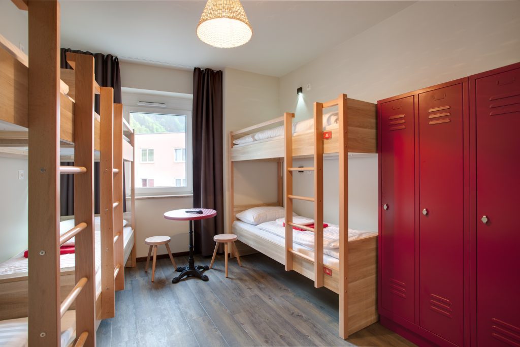 Dormitorio con letti a castello in legno, armadietti rossi, tavolino e sgabelli