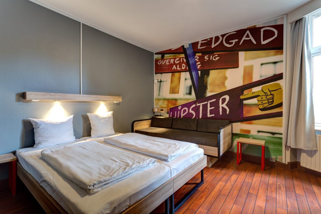Bright and clean twin room at MEININGER Hotel Copenhagen with fresh white bedding, warm wood floors and a bold street art mural on the wall
