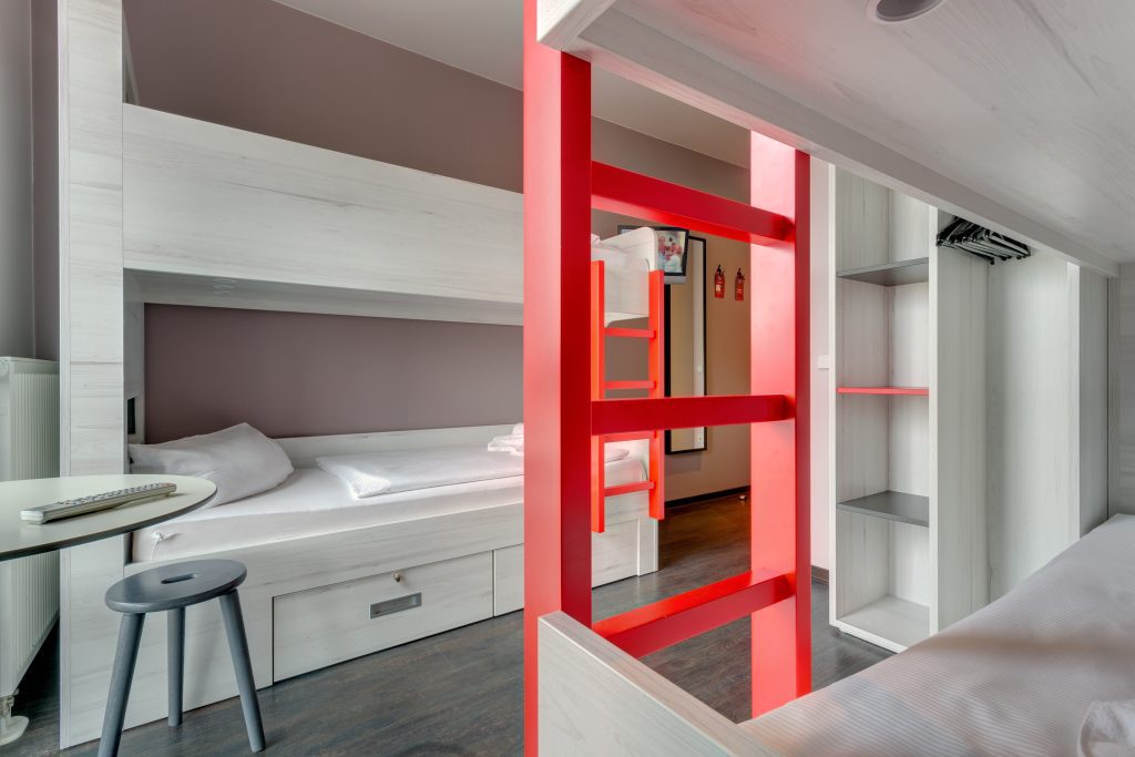 Weißer Schlafsaal mit rot gerahmten Etagenbetten und eingebautem Stauraum