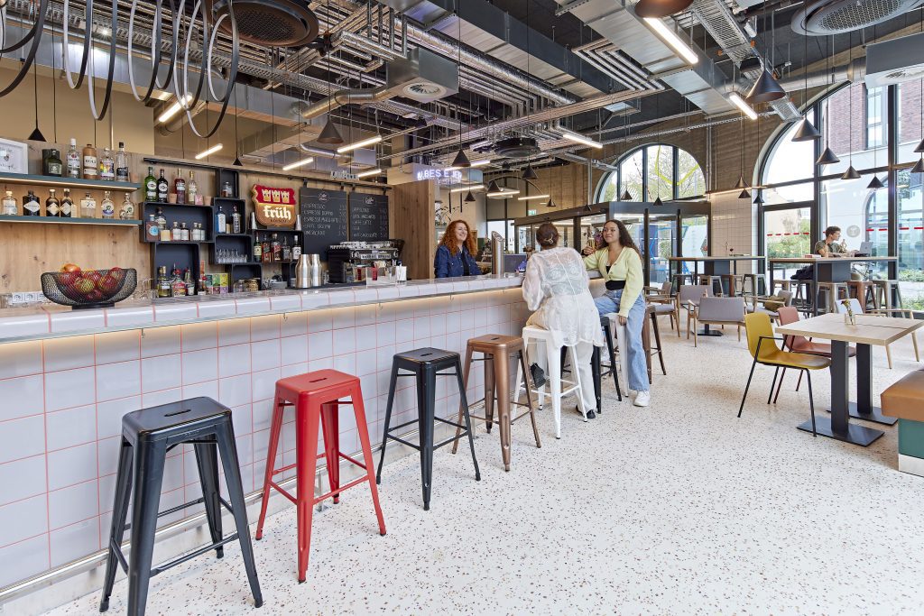 Lebhafte Hotelbar mit Barhockern und offenem Deckendesign bei MEININGER