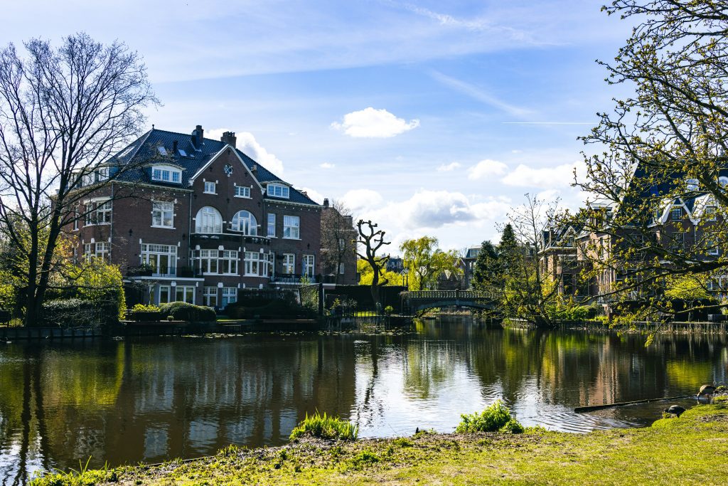 Amsterdam mit Kindern: Vondelpark Amsterdam mit Teich und typischen Amsterdamer Häusern an einem Sonnentag