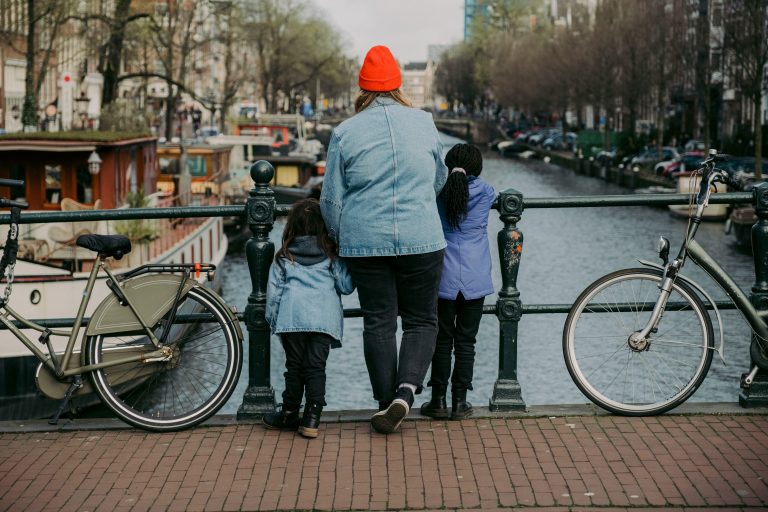 A woman with 2 kids from behind on a bridge looking at an Amsterdam's canal