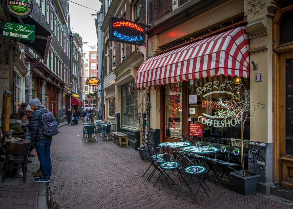 Best coffee shops in Amsterdam: A coffee shop on a street with neon signs and outdoor seating