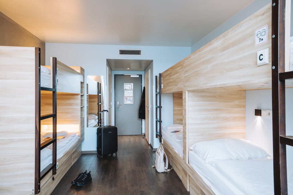 Helles Schlafsaalzimmer mit Holzetagenbetten, weißer Bettwäsche und Koffer