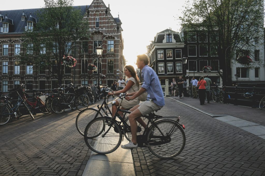 Bike rental Amsterdam: Couple cycling across a charming cobblestone street in Amsterdam