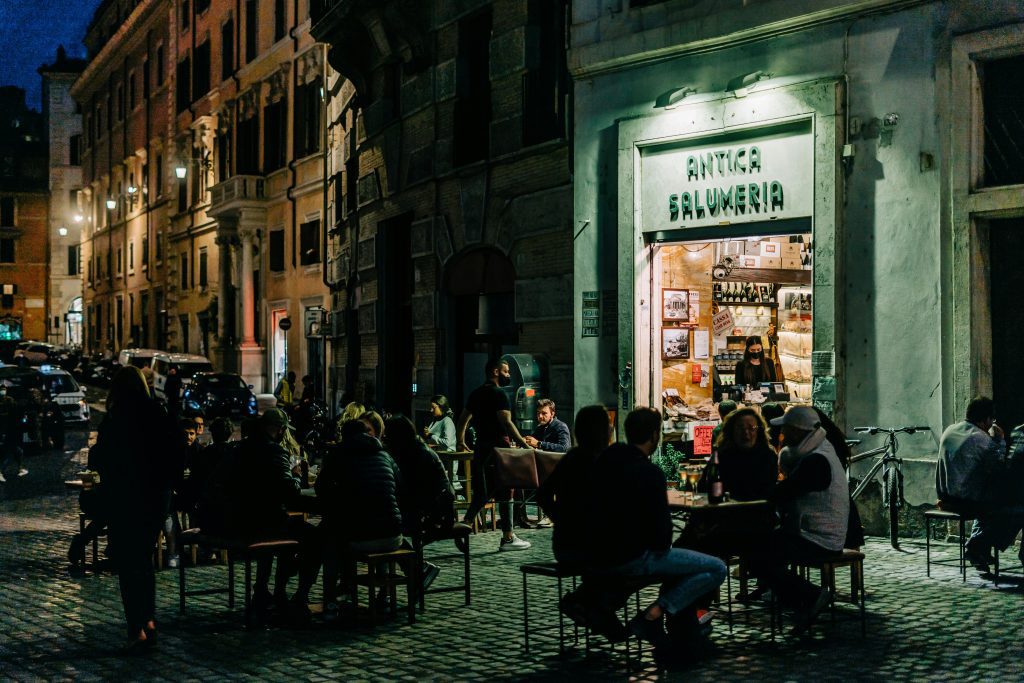 Rom guenstig: Einheimische genießen den abendlichen Aperitivo vor einer traditionellen Salumeria in Rom