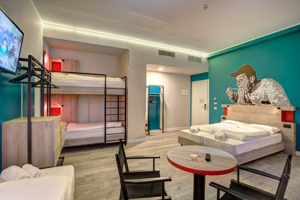 Helles Hotelzimmer mit Etagenbett, Doppelbett, türkisfarbenen Wänden und einem Street-Art-Wandbild