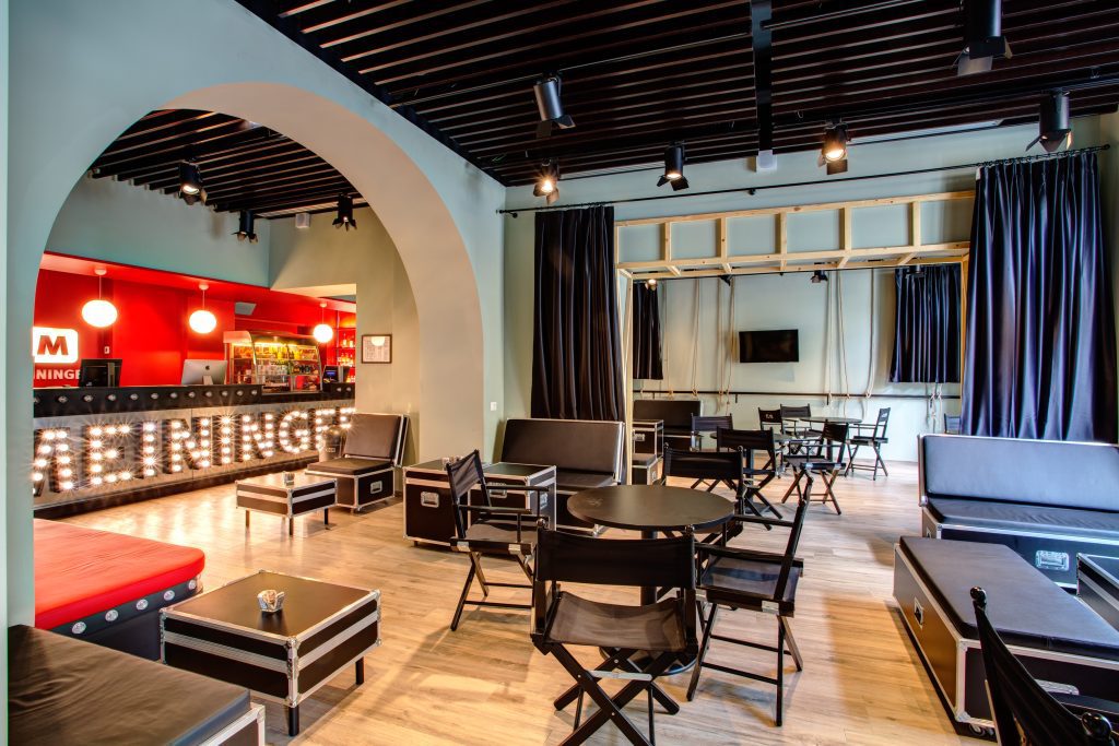 Geräumige Lounge mit Regiesesseln, Roadcase-Tischen, einer Bar und Leuchtbuchstaben mit MEININGER-Schriftzug