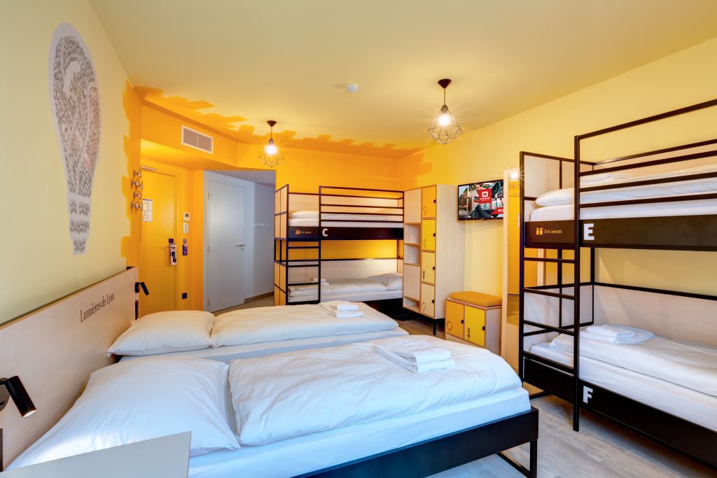 Yellow dorm room with a double bed and bunk beds