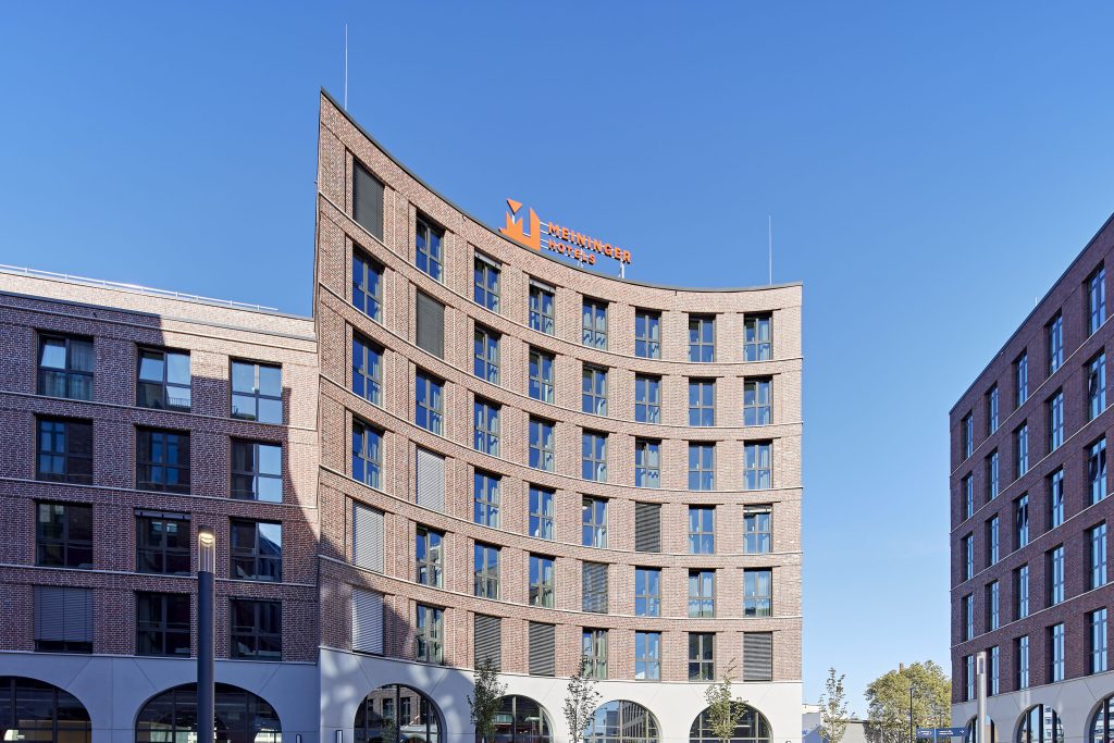 MEININGER Hotel Köln West exterior with orange logo under blue sky