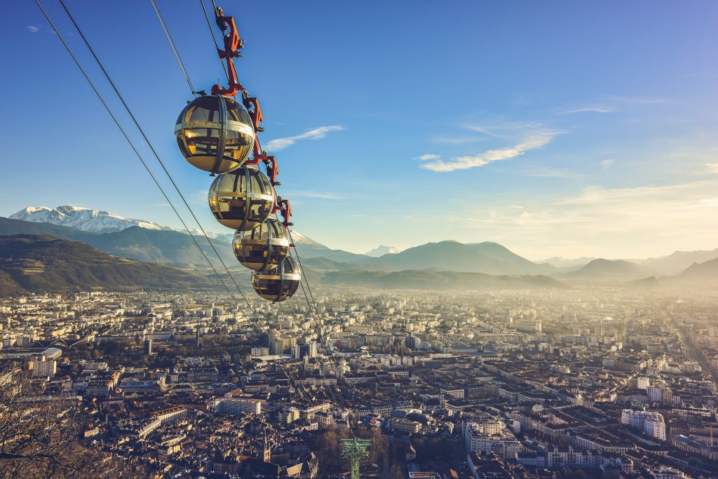 Things to do around Lyon: A cable car descends towards a valley with buildings, surrounded by mountains.