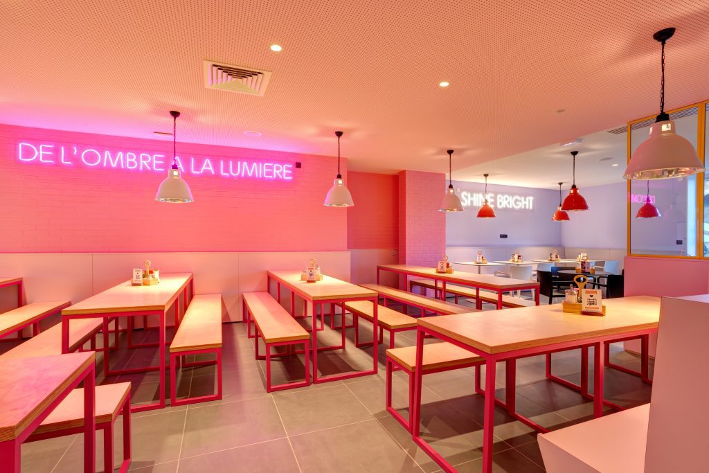 Pink breakfast room with neon on the wall, tables and benches