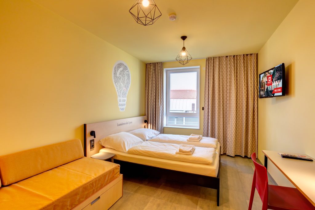 Yellow double room with sofa, desk and a big window