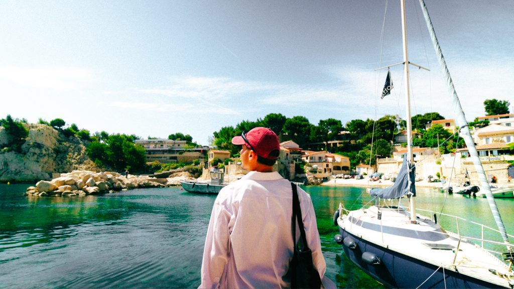 Backpacking Frankreich kleinem Budget: Backpacker blickt auf einen sonnigen französischen Hafen mit Segelboot