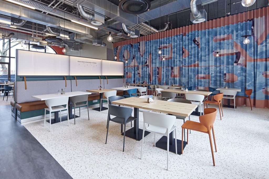 Breakfast area with tables, chairs and an artwork curtain at MEININGER Köln West
