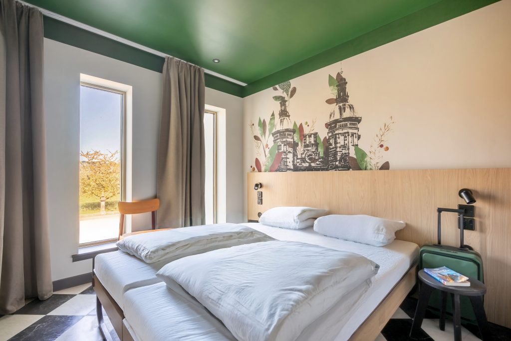 Zwei Einzelbetten mit weißer Bettwäsche, Holzkopfteil, grüne Zimmerdecke, Wandbild mit Turm