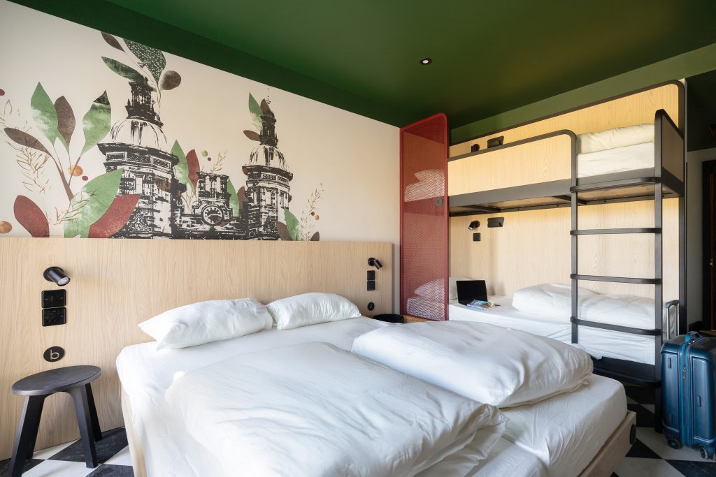 Hotelzimmer mit Doppelbett, Etagenbett und einem Wandbild mit Kirchtürmen