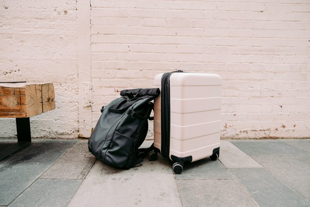 Luggage storage Berlin: Cream suitcase and black backpack resting against a brick wall outdoors